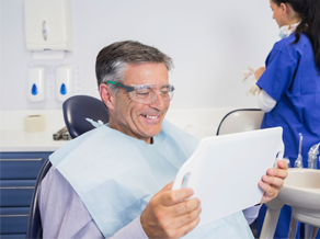 older man in dental chair examining his smile in a mirror