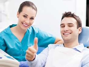Dental assistant next to chair with patient smiling and giving thumbs up