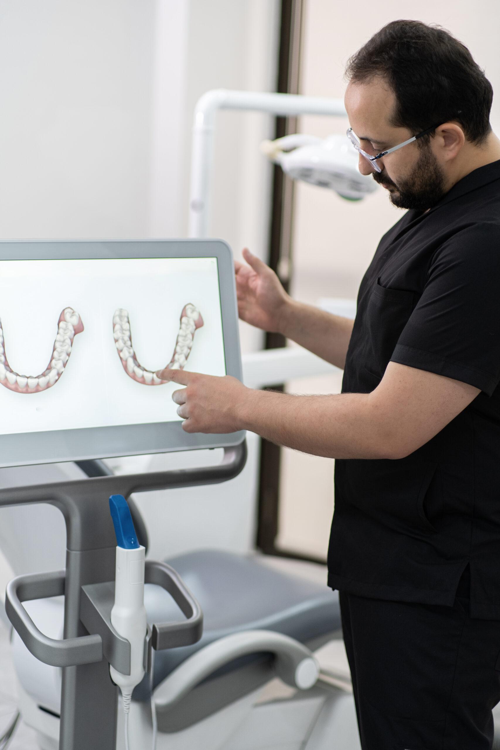 Specialist in uniform pointing to jaws models on computer screen using alternative teeth treatment dentist using UV light on a patient's teeth